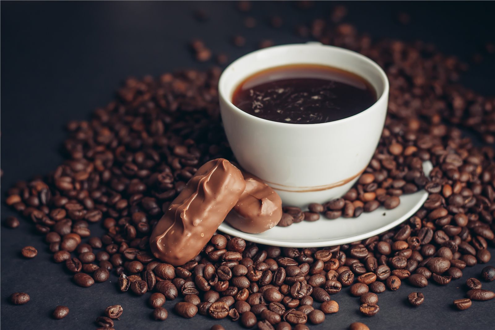 Cup of coffee surrounded by dark roasted coffee beans